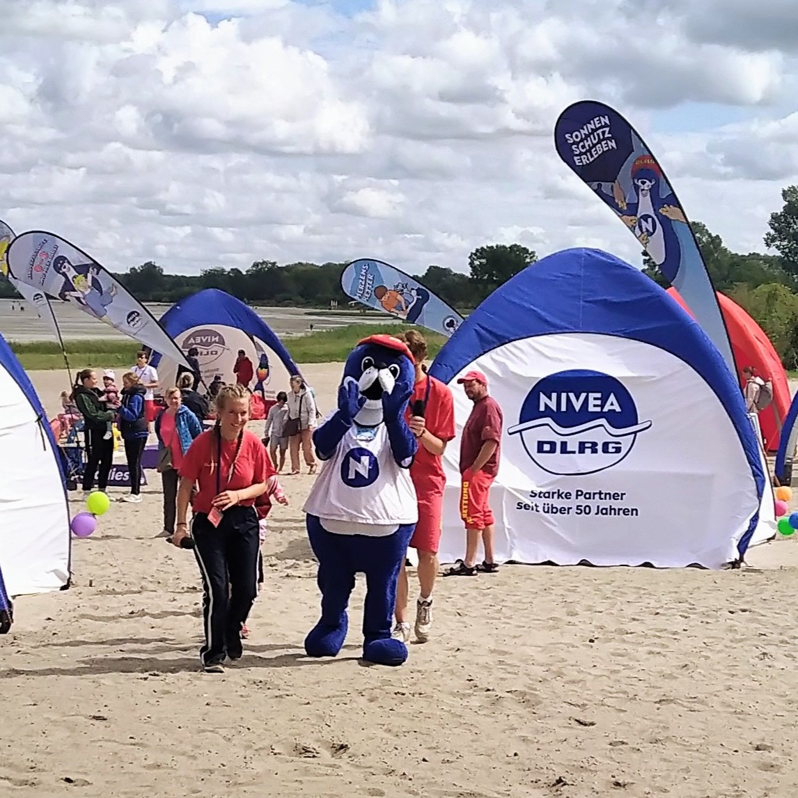 Zelte von DLRG und Nivea und das Nivea-Maskottchen, ein blauer Seebär aus Plüsch, am Strand