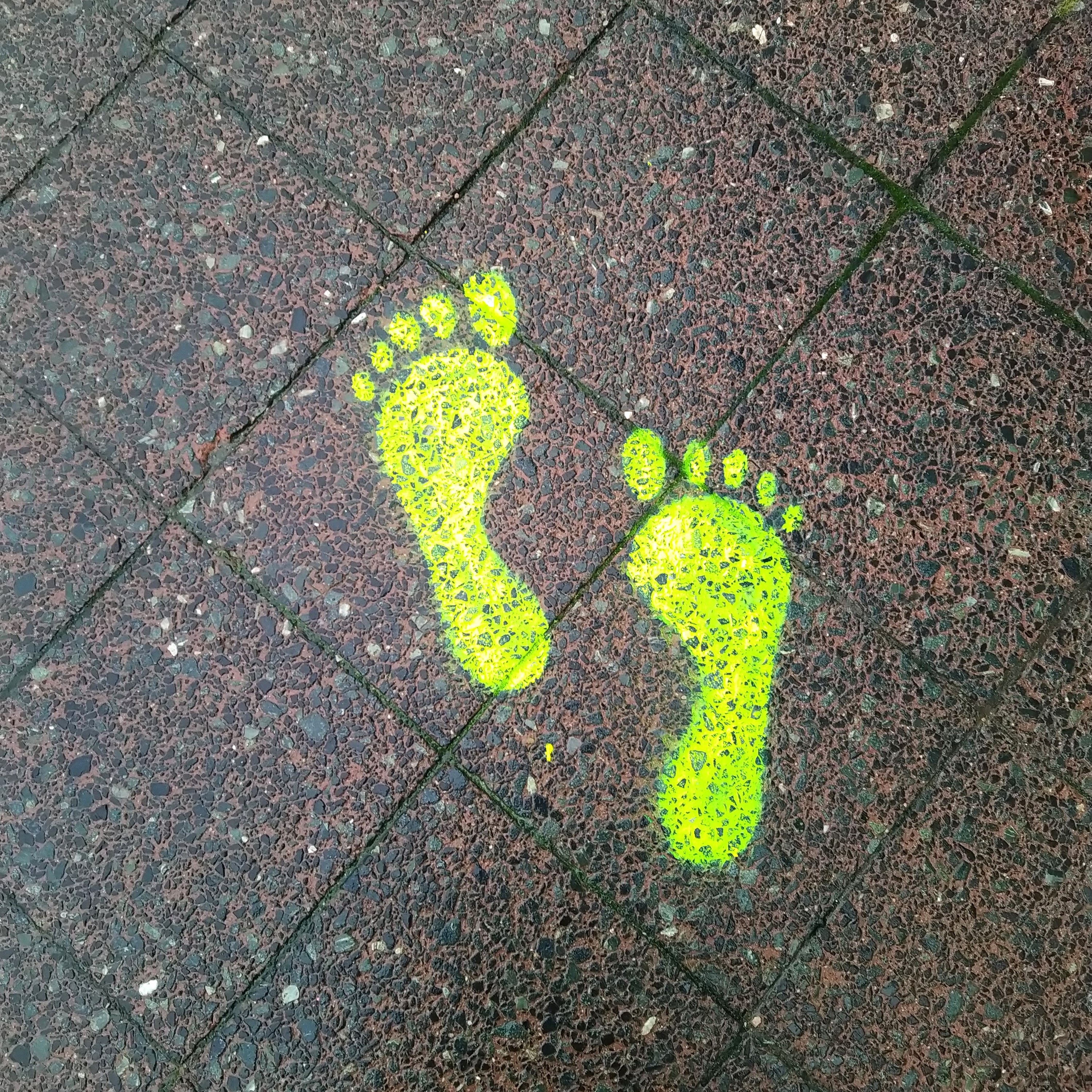 Neongelb-leuchtende Fußspuren auf dem Asphalt.