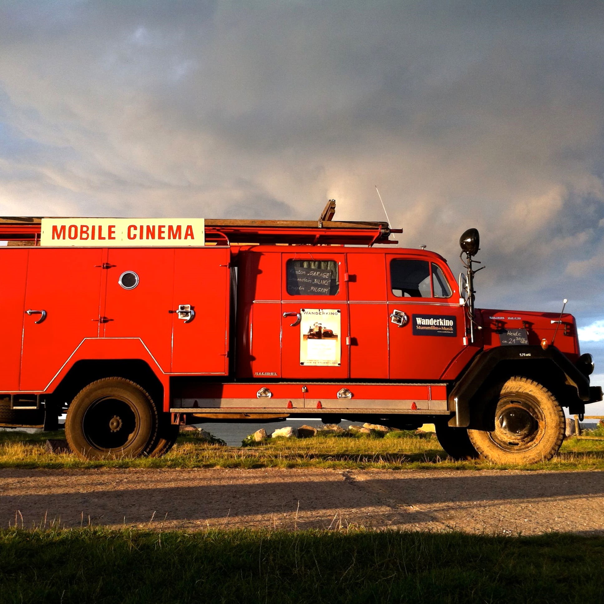 An old red fire engine converted into a traveling cinema with the sign 