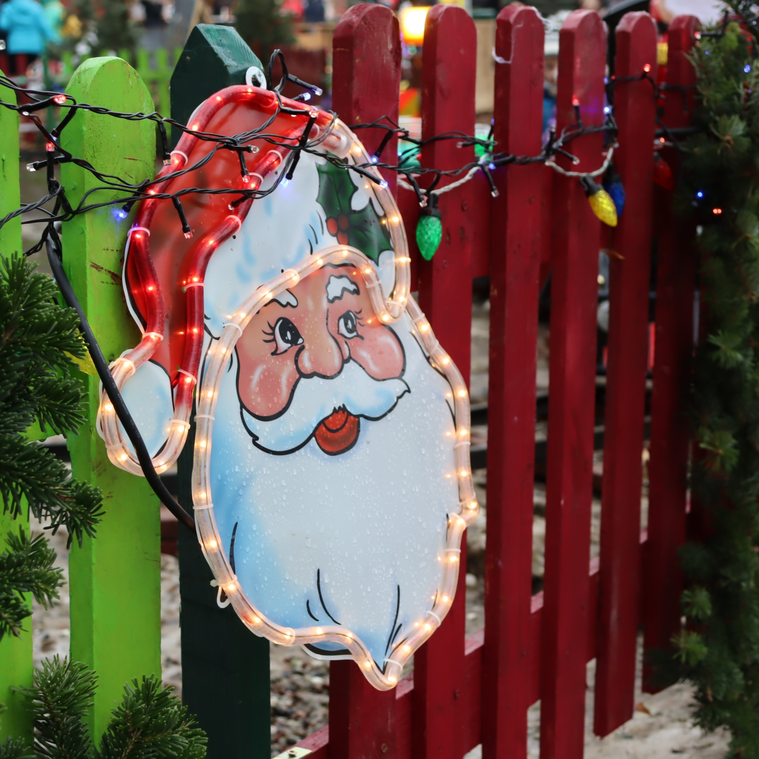 Figur eines Weihnachtsmannkopfes mit Lichterkette an einem Zaun.